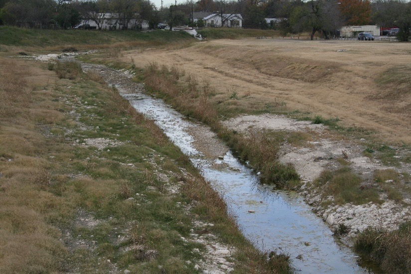 Small creekline surrounded by minimum vegetation, rocks, and undeveloped land.