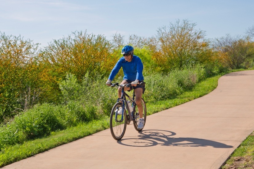 Man rides his bike along a walking trail surrounded by lush vegetation.