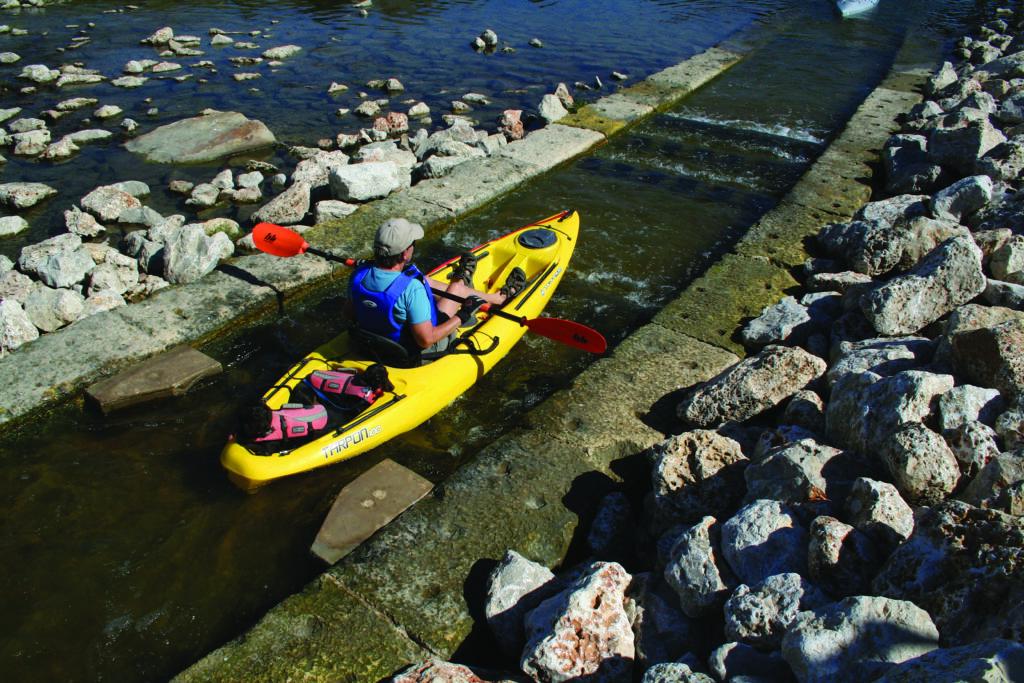 A man in kayak enters the San Antonio River through a waterway entry point.