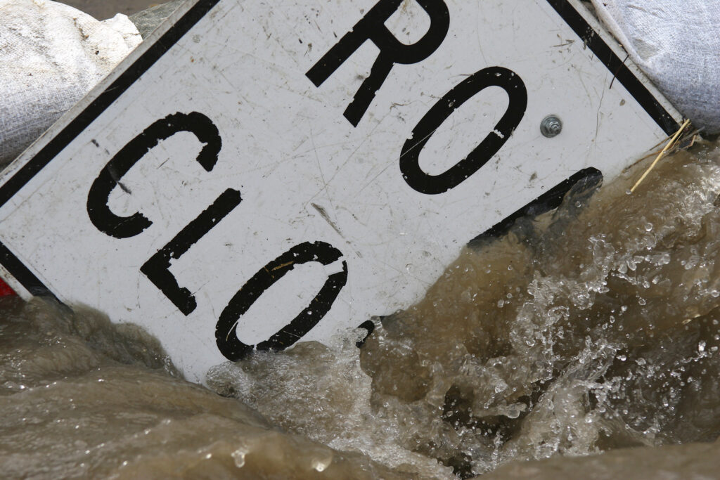 "Road Closed" street sign submerged by flood waters.