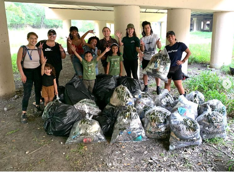 Team stands triumphantly next to trash collected at local park. 