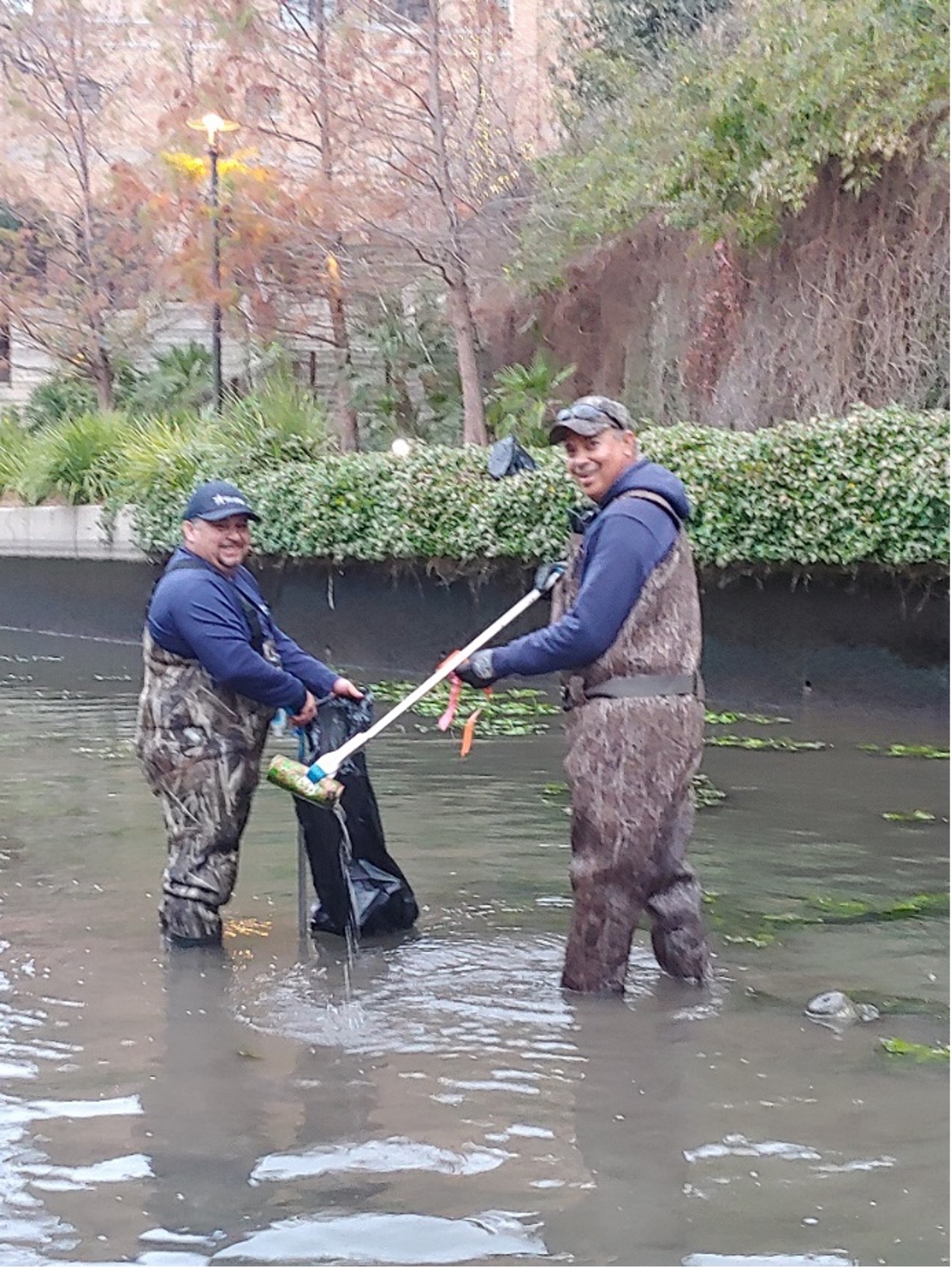 two riparian technicians pull trash out of river during river draining.