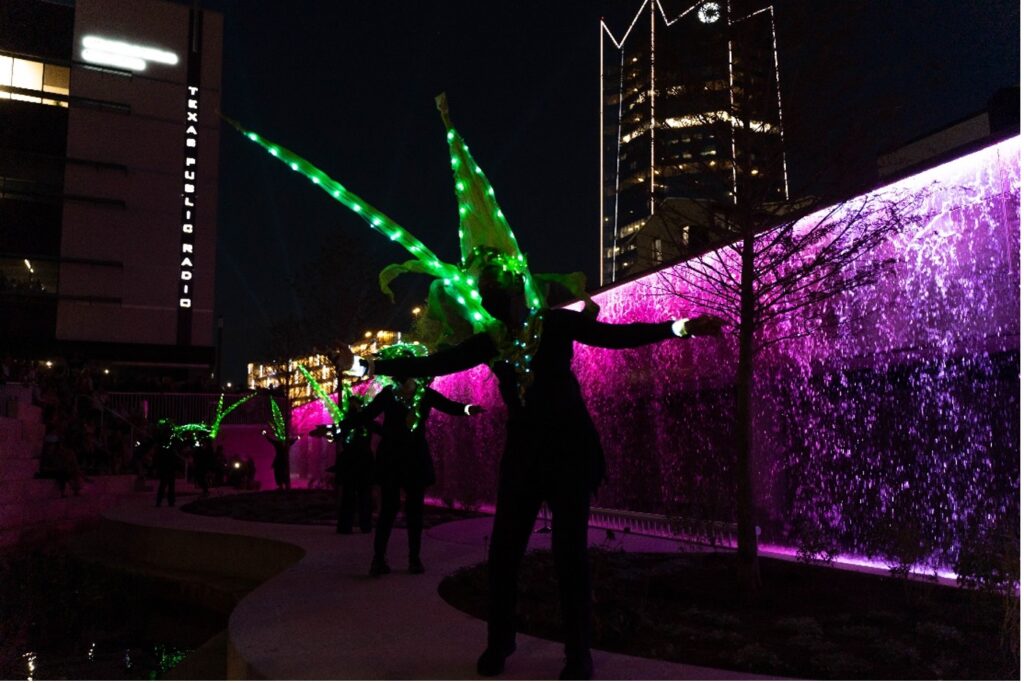 Dancers in light up costumes perform in front of the new interactive art piece STREAM