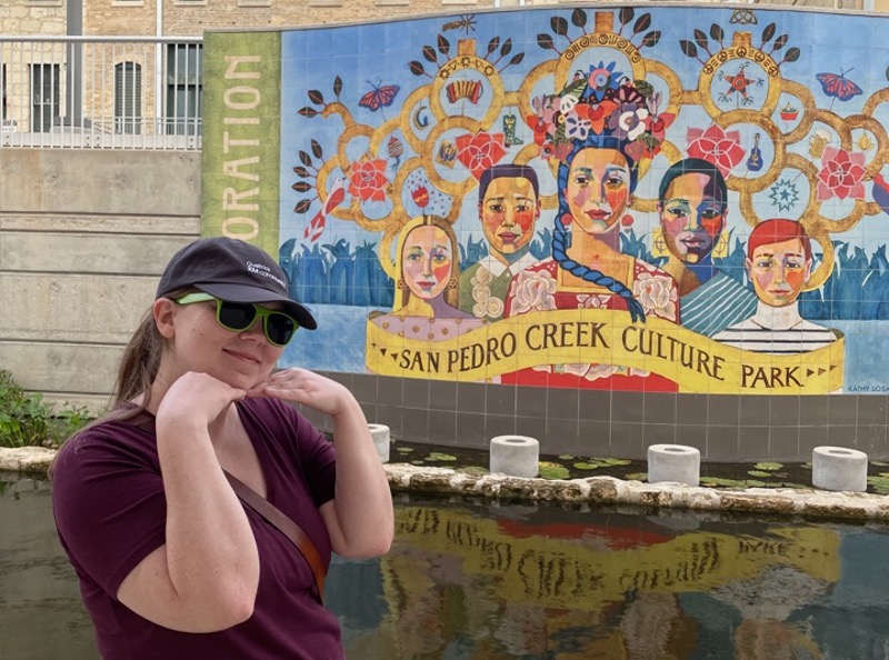 A woman takes a photo in front of large tiled mural 