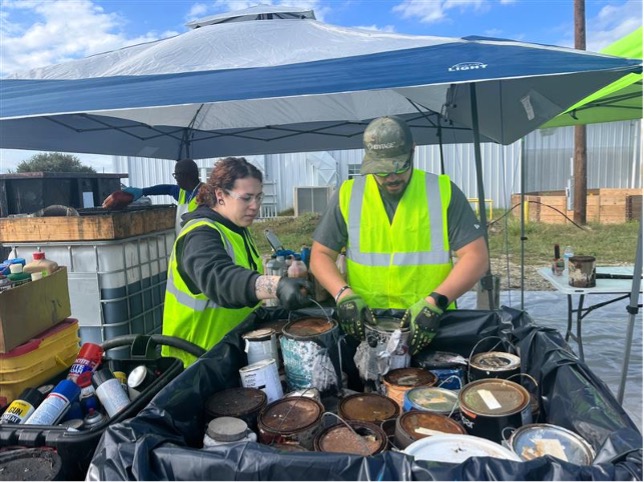 Two workers sort through old paint cans during hazardous household waste collection event