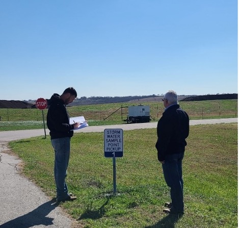Two men out in the field near sign that reads 