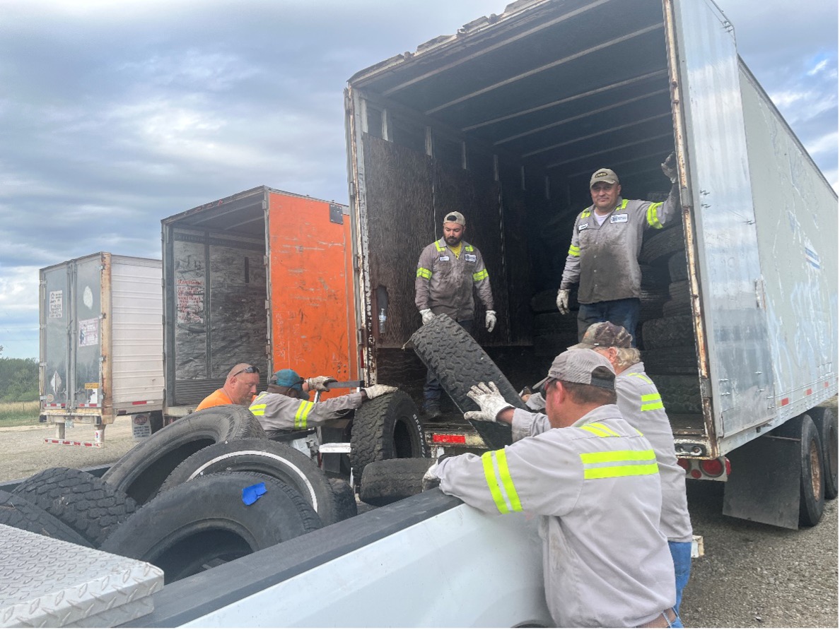 Workers load old tires into the back of collections truck.