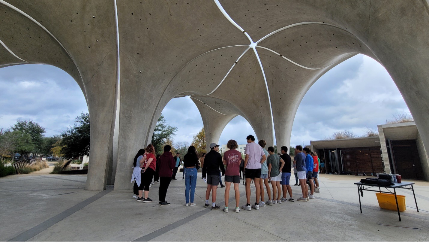 Students gather around a circle under park pavilion.