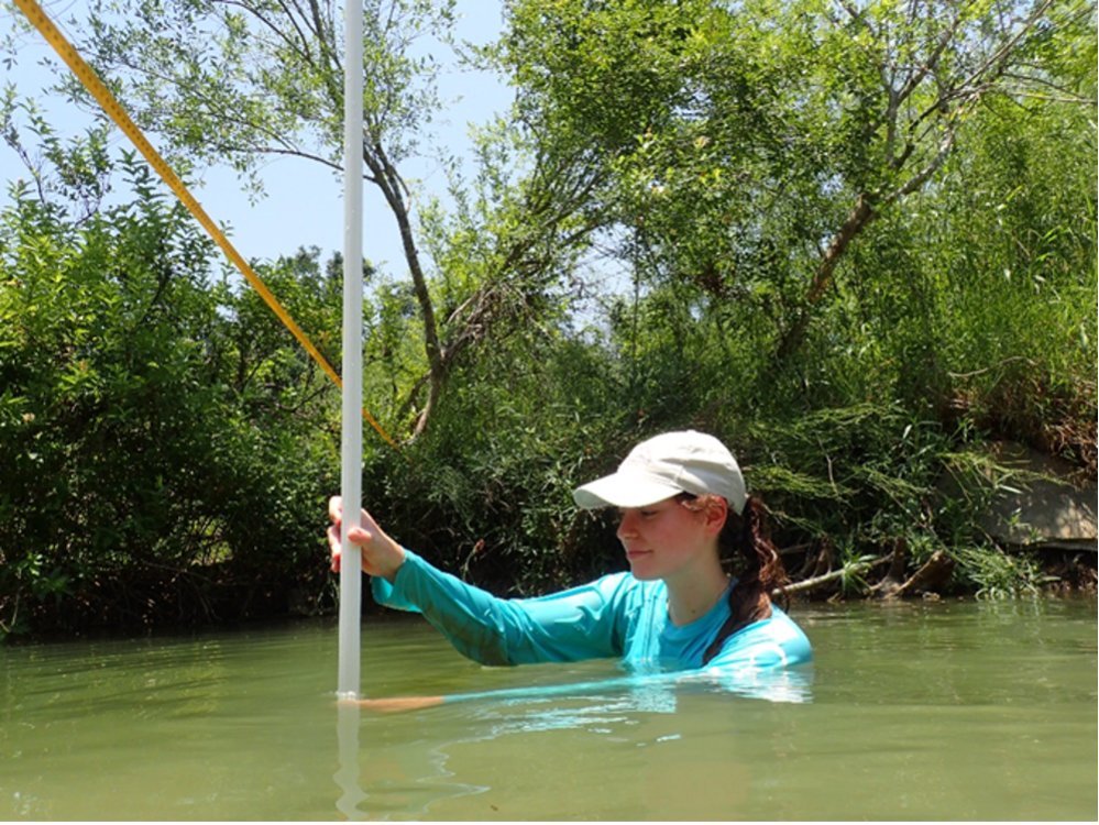 Young woman measuring dept in the river.