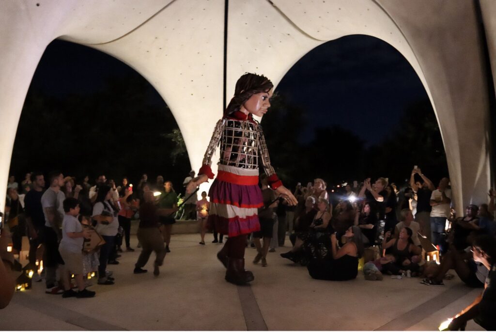 A tall puppet under a pavilion surrounded by people.