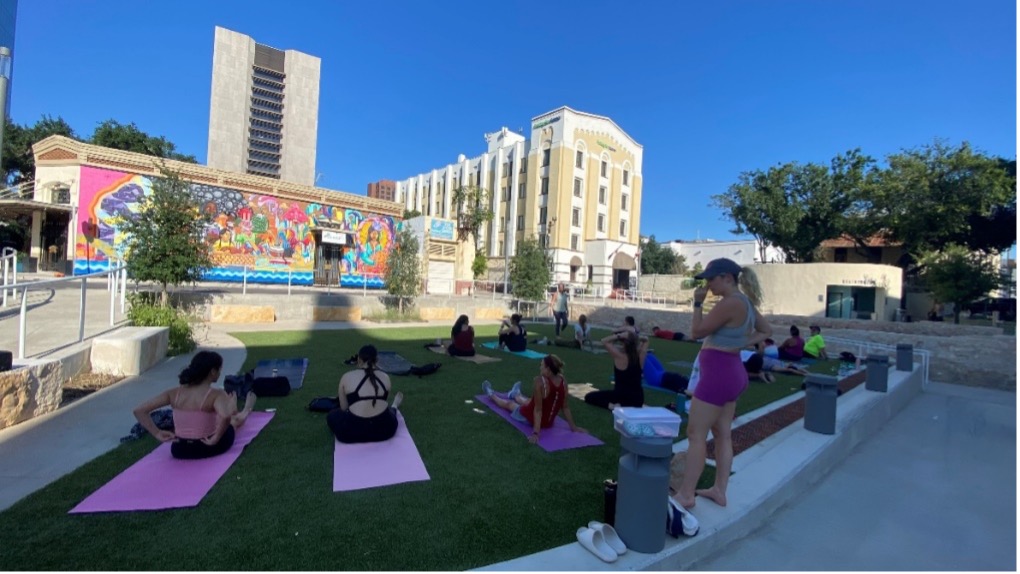 A group of people sit on yoga mats outside.