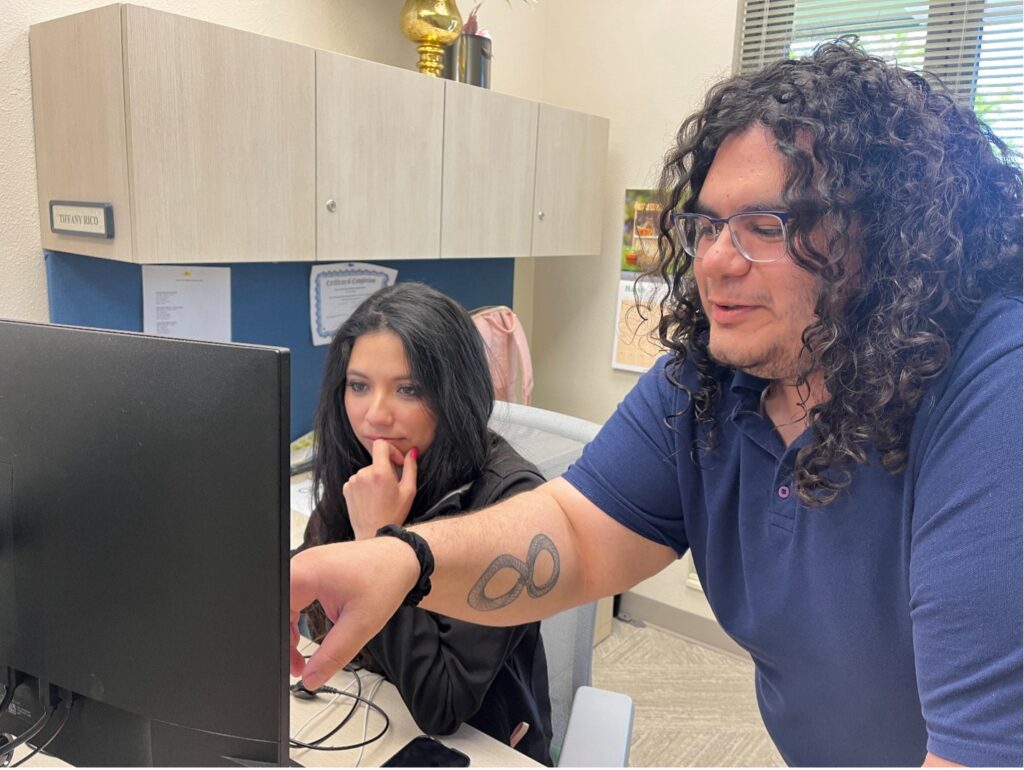 A man points to a computer assisting woman.