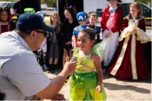 A small child dressed as tinkerbell talks on the mic to an adult man during Fall Festival Costume contest.