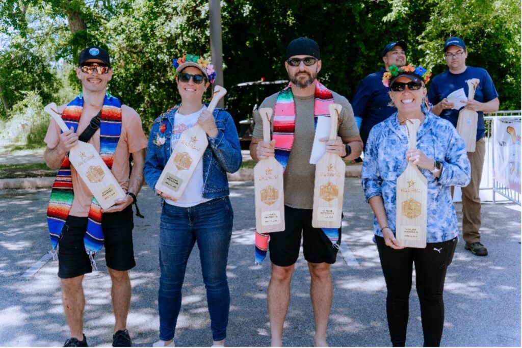 Four people stand proudly with their paddling trophies after paddling race.