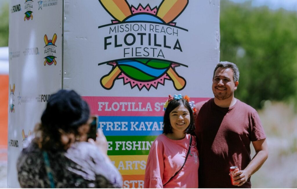 A couple poses next to the Fiesta Flotilla Sign