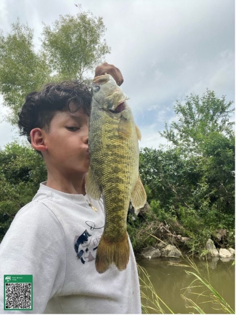 A young boy kisses his freshly caught bass