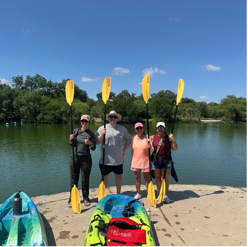 A group of people stand with kayak paddles near the San Antonio River