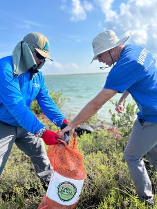 Two River Warriors add trash to a bag during a cleanup event.