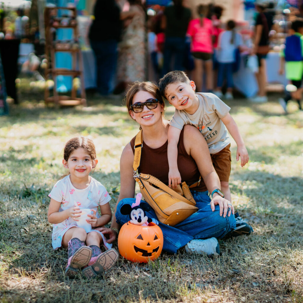 A woman and two children sit together on the ground during the Fall Fest event.