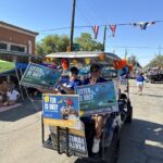 Two people sit in the back of a golf cart holding "Litter Is Ugly" signage